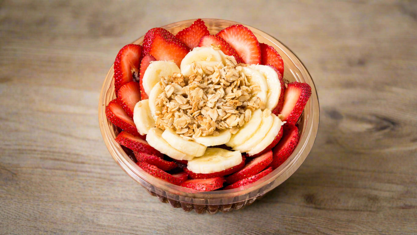 Fruit salad with strawberries, bananas, and granola in a clear bowl on a wooden surface, featuring the Doordash logo.